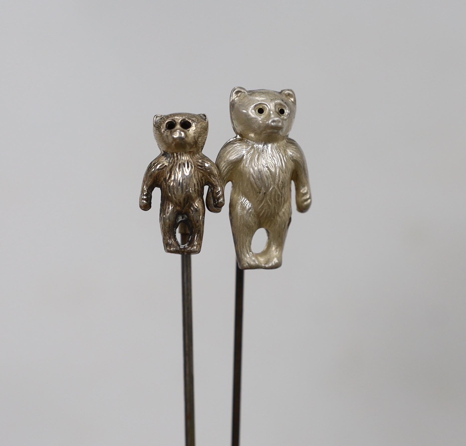 Two Edwardian hat pins with silver hallmarked teddy bea tops, and a silver 1960's teddy bear rattle